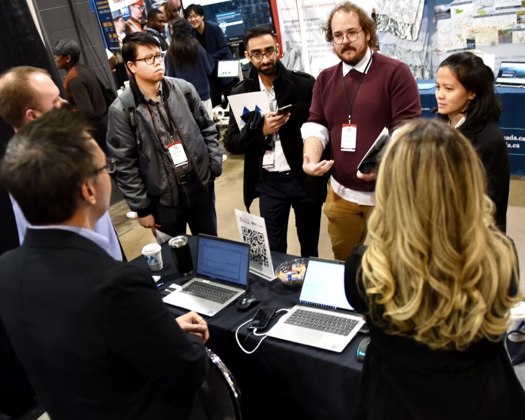 A crowd of delegates gathers around laptops at a busy exhibitor stand