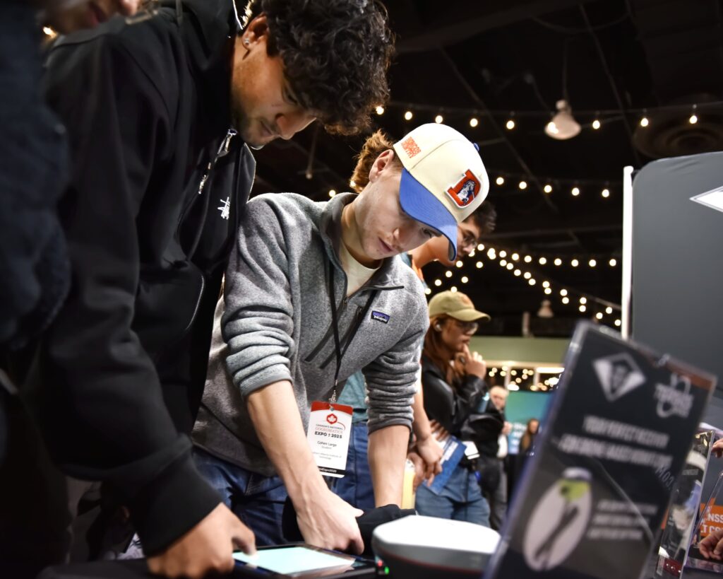 Delegates lean in to test a handheld device at an exhibitor stand