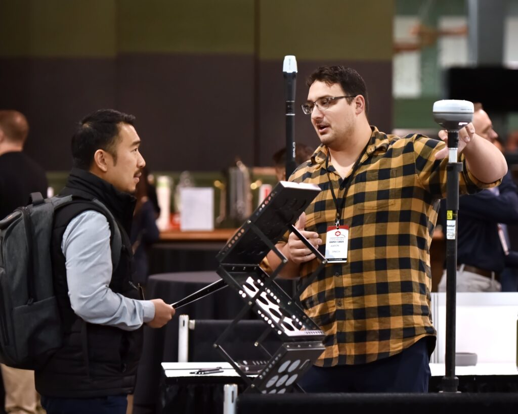 An exhibitor demonstrates a field controller and GNSS pole to a delegate