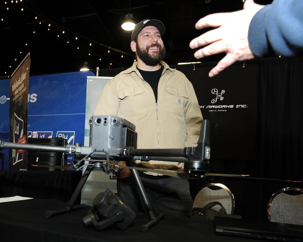 An exhibitor gestures while presenting a LiDAR-equipped drone at his stand
