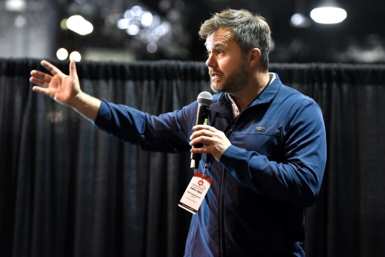 A presenter throws an arm wide while speaking with a handheld microphone